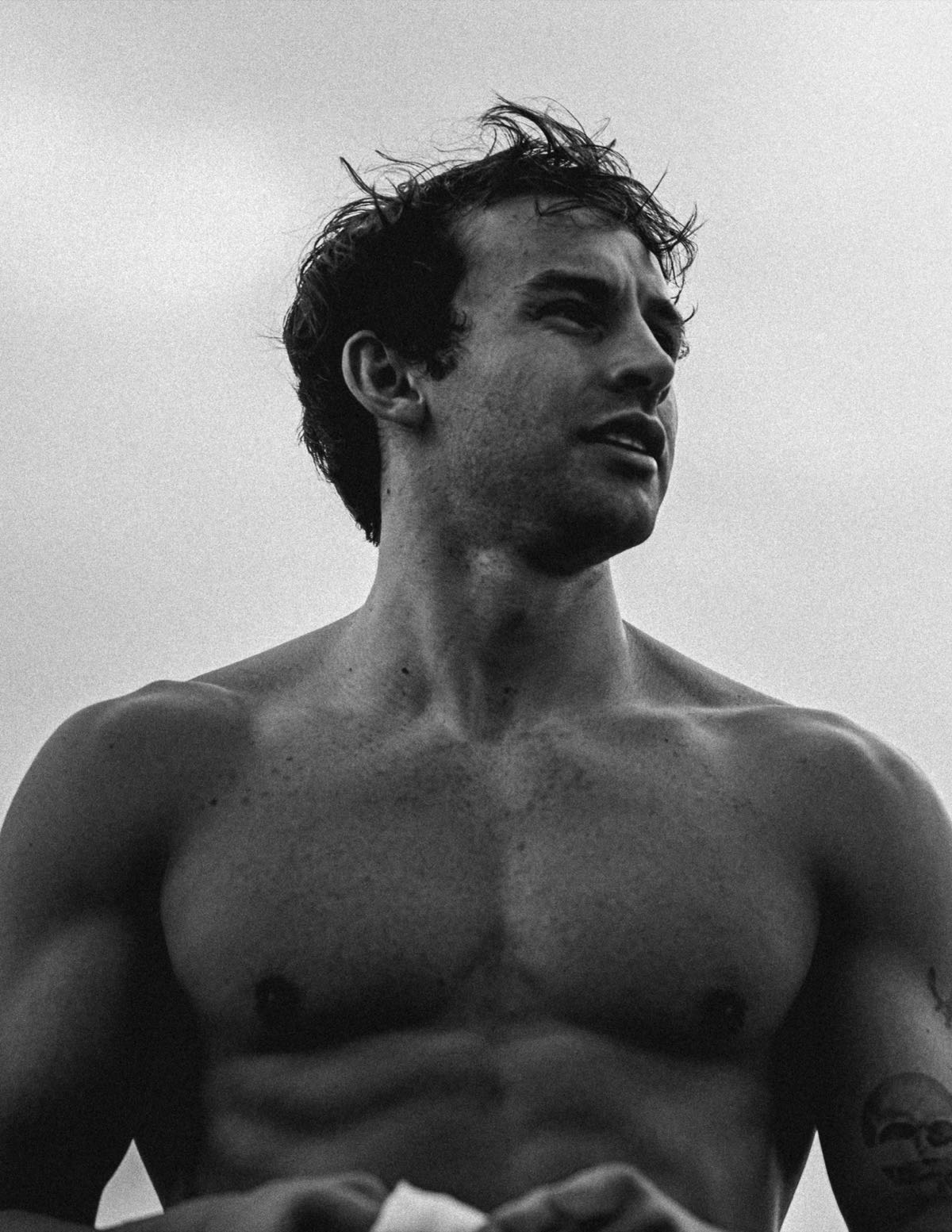 Anthony shirtless outdoors in black and white, looking off under a grey sky