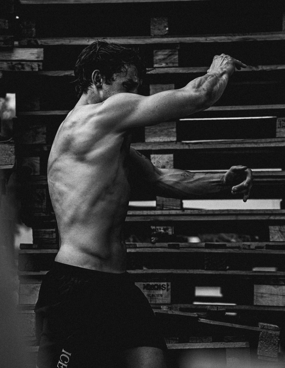 Anthony in black and white, fists up in a boxing stance in front of wooden shelving