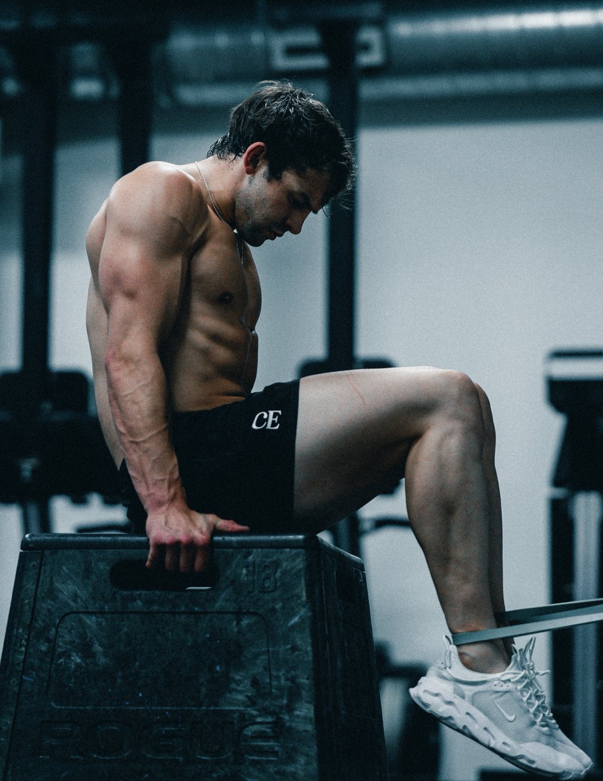 Anthony seated on a plyo box, one knee lifted against a band, head down